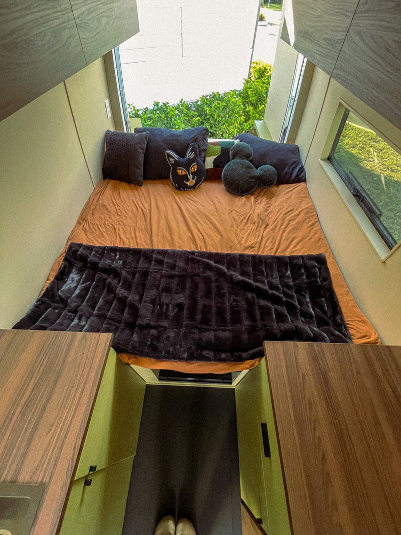 Experience a cozy rv rental! This modern sleeping nook features an orange bed, plush blanket, fun pillows, and scenic windows. — photo 6