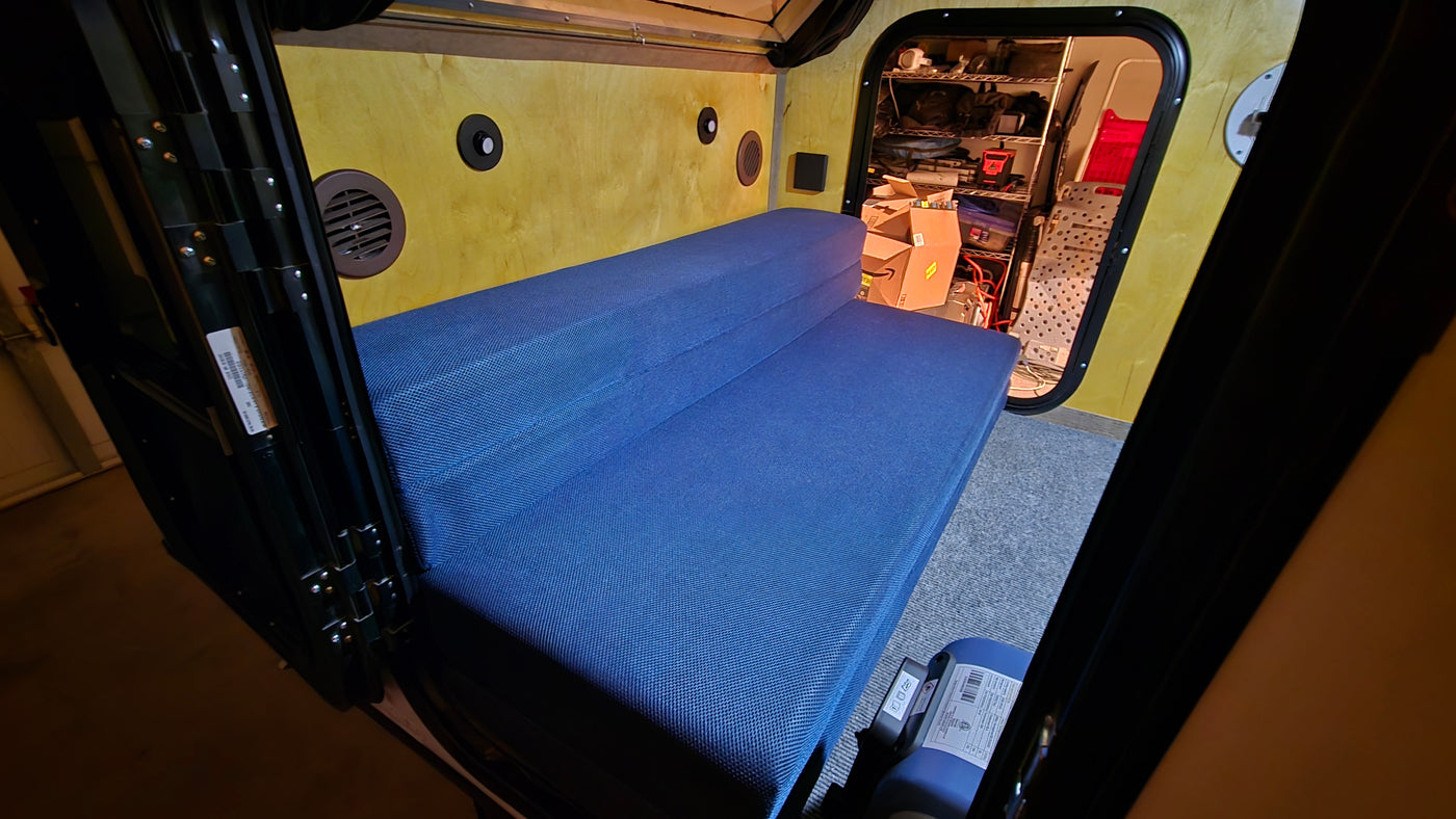 RV rental: Interior of a small camper with a blue folding mattress, wood-paneled walls, and organized rear storage. — photo 3