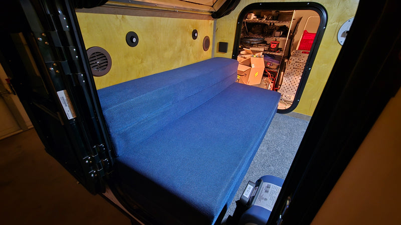 RV rental: Interior of a small camper with a blue folding mattress, wood-paneled walls, and organized rear storage. — photo 3