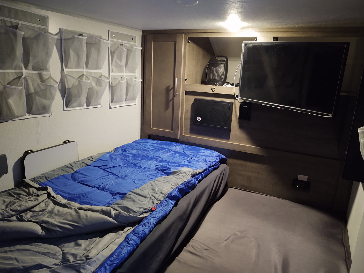 Cozy rv rental space with sleeping bag bed, wall organizers, built-in cabinets, a portable heater, and a TV.