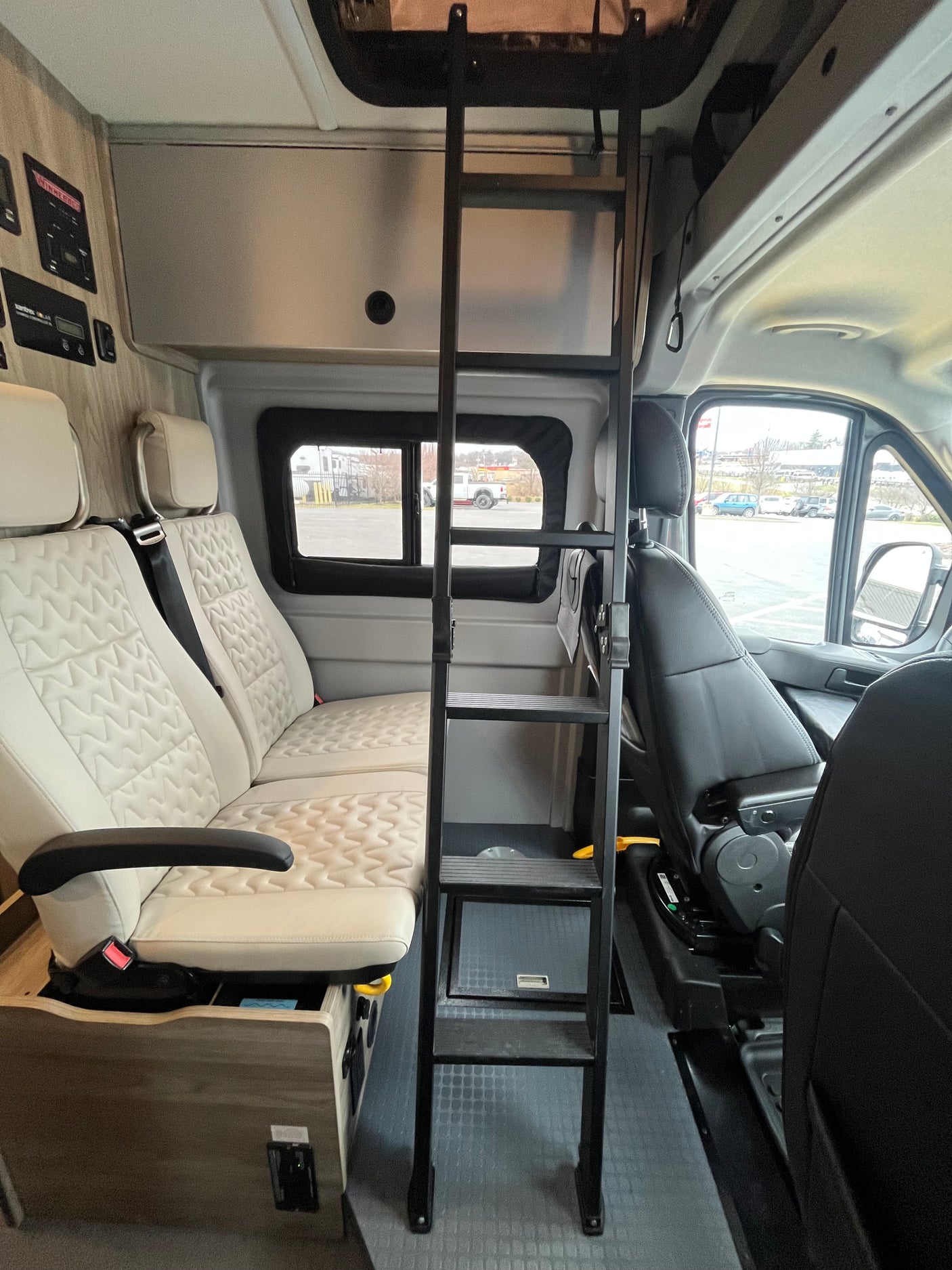 Inside an RV rental, featuring quilted passenger seats, an overhead bunk access ladder, and a side control panel, perfect for travel.