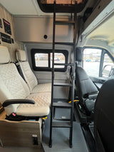 Inside an RV rental, featuring quilted passenger seats, an overhead bunk access ladder, and a side control panel, perfect for travel.