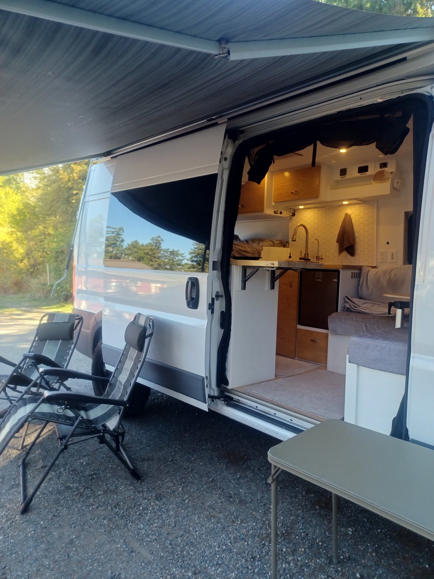 Enjoy comfort outdoors with this RV rental! Open campervan with interior kitchen, seating, awning, and camping chairs.