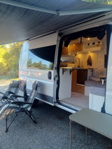 Enjoy comfort outdoors with this RV rental! Open campervan with interior kitchen, seating, awning, and camping chairs.