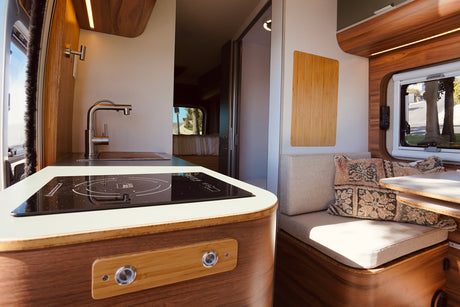 Inside a bright RV rental, see the modern kitchen with wood accents, induction cooktop, and comfy dinette.