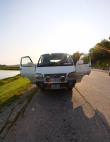 White Toyota van, like an RV rental, open doors on an Oregon road trip. Parked by a sunny lake.