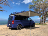 This blue camper van, an ideal rv rental, has an awning extended by the beach, perfect for oceanfront relaxing.