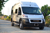 Front view of a silver Winnebago camper van on a RAM ProMaster chassis, ideal for rv rental, parked on gravel.