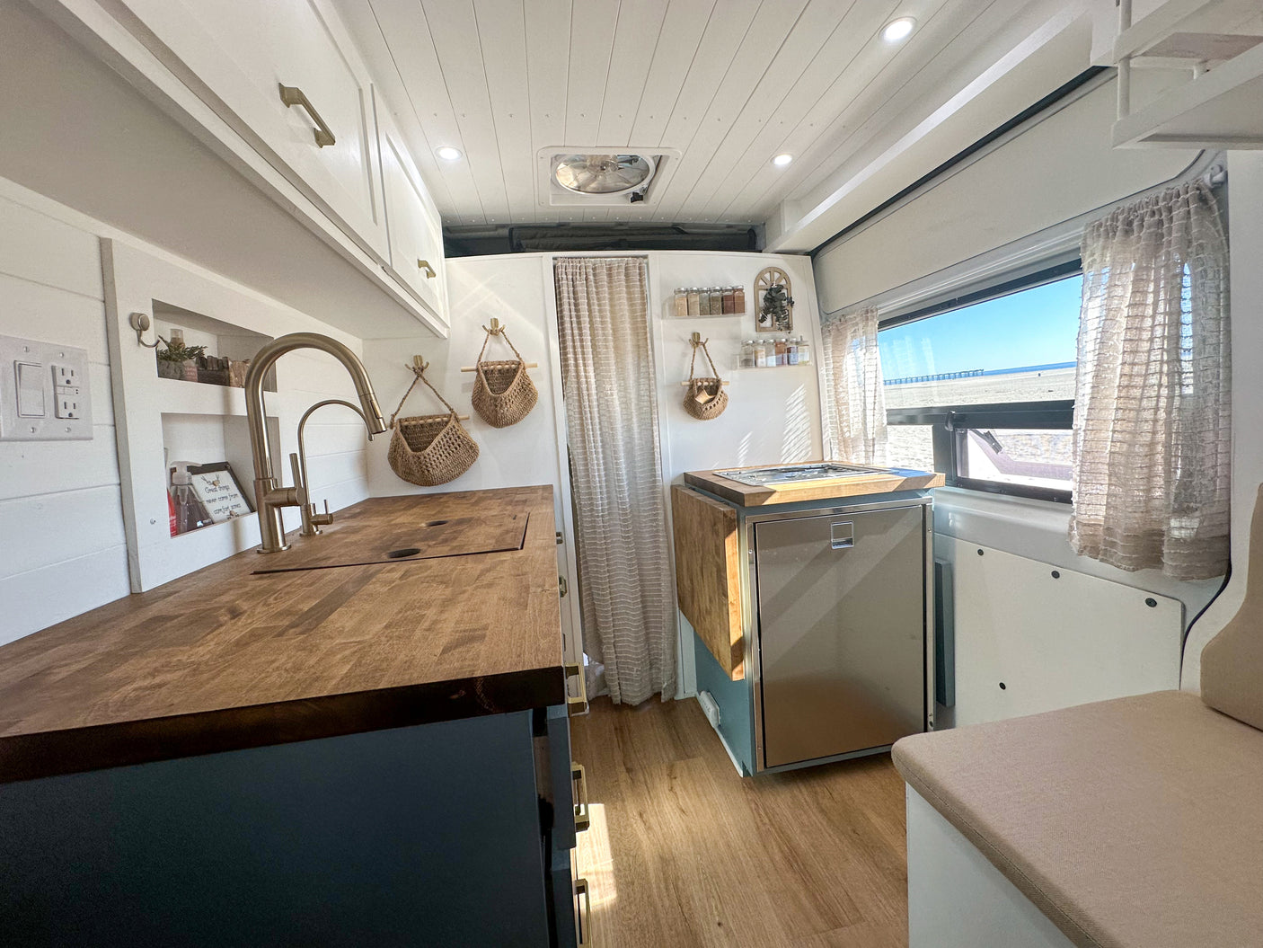 RV rental interior: modern kitchenette with wood counters, golden fixtures, and a bright beach view window.