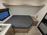 RV rental interior: A compact sleeping area with a grey bed, emergency exit window, and small sink. Ideal for road trips.