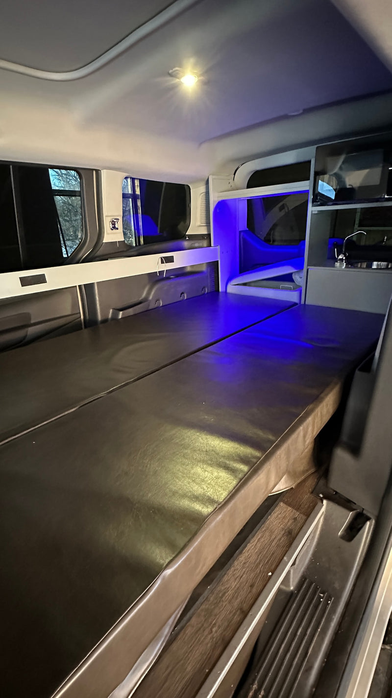Inside an RV rental campervan: a cozy interior with a bed, windows, overhead lighting, and a compact kitchenette with blue light. — photo 5