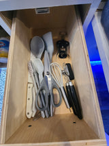 RV rental kitchen drawer stocked with compact essentials: corkscrew, can opener, whisk, spatulas, and knives.