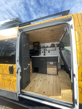 Inside this rv rental: spacious camper van interior with modern kitchen, wood floors, ceiling, & convenient hooks.