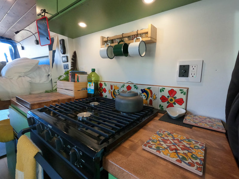 Cozy rv rental kitchen with a stove, kettle, and decorative tiles, perfect for cooking on the go. — photo 11
