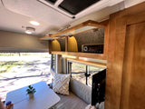 Cozy RV rental interior showing open overhead cabinets, a media player, dinette, and bright windows with outdoor views.