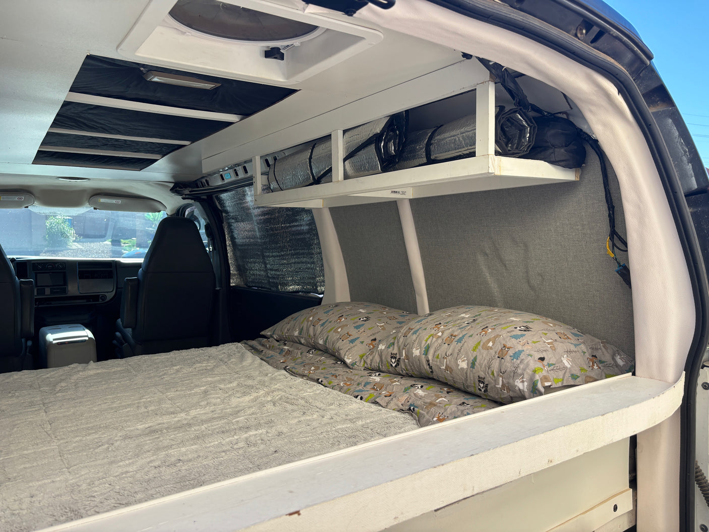 Inviting rv rental camper van interior: a cozy bed, custom overhead storage, and driver's area are visible.