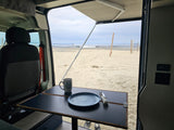 Experience beach life in an RV rental! Inside a campervan, table set for breakfast with ocean & volleyball net view.