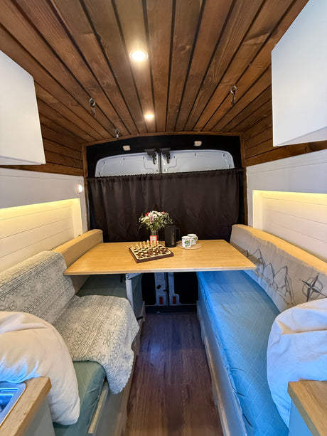 Cozy rv rental interior featuring wooden ceiling, dining area with chess set & flowers, and built-in benches.