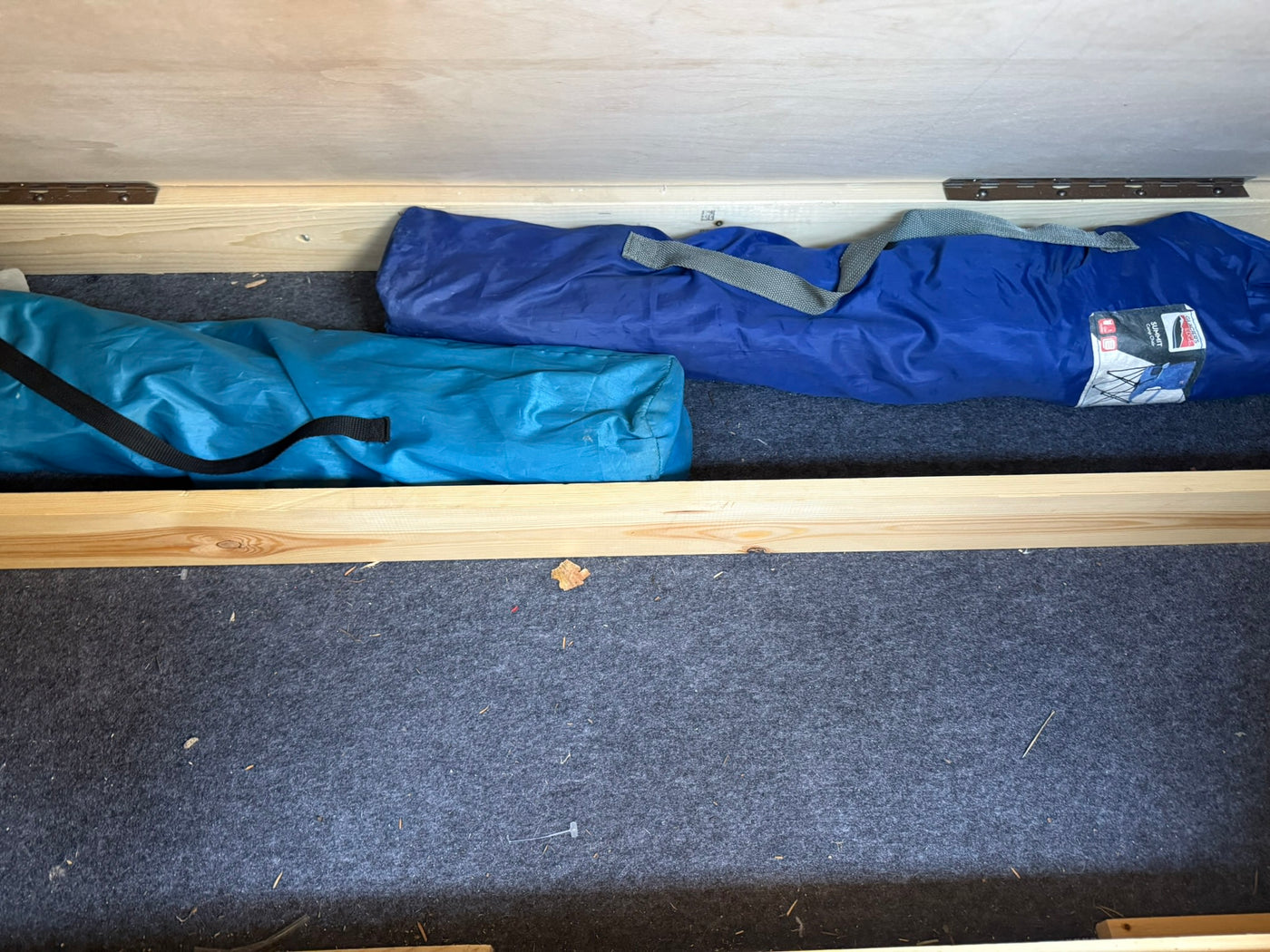 Inside an RV rental storage compartment, two blue bags of portable camp chairs are neatly stowed on a dark grey carpeted floor. — photo 9