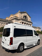 White Mercedes Sprinter RV rental, a luxury camper van, stands before a grand, classical-style building under a clear blue sky.