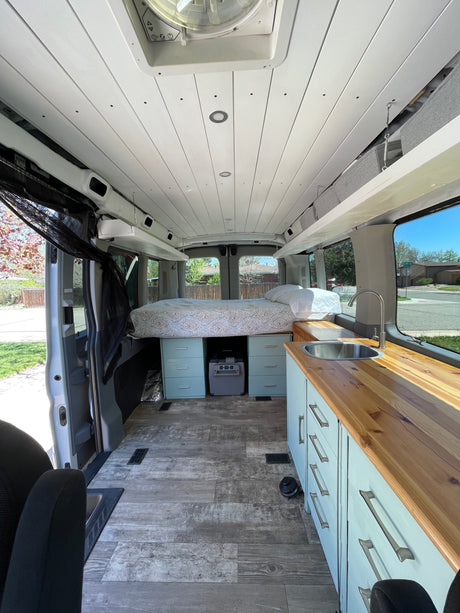 This RV rental van interior features a comfy bed, kitchen counter with sink, and ample storage for your road trip comfort.