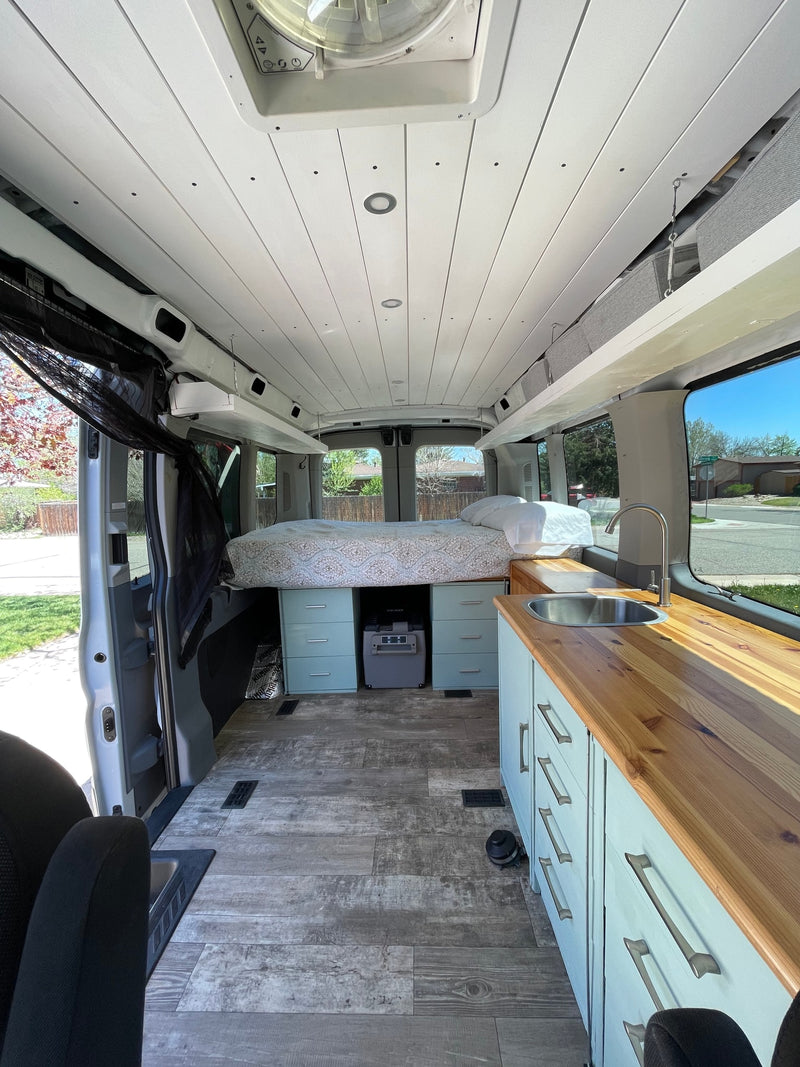 This RV rental van interior features a comfy bed, kitchen counter with sink, and ample storage for your road trip comfort. — photo 3