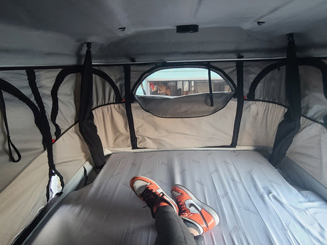 Enjoying the view from a comfortable mattress inside an RV rental or rooftop tent, complete with person's feet in sneakers.