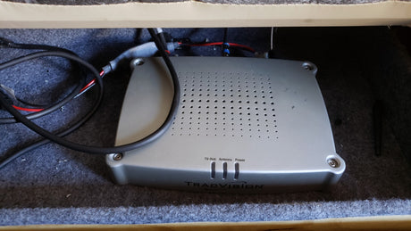 RV rental's TracVision TV-Hub satellite system, with wires, in a carpeted storage area.
