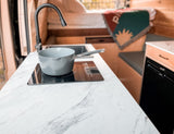 Compact kitchen in an RV rental featuring a white marble-look counter, induction cooktop with saucepan, and modern faucet.