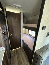 Inside an RV rental: view of bunk beds, a private door, and kitchen space, highlighting compact living and travel comfort.