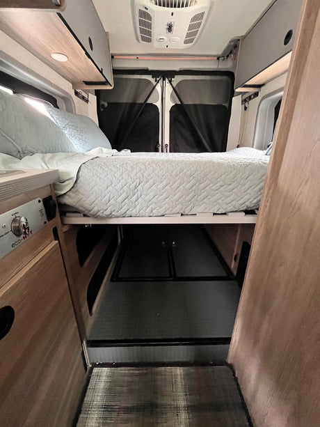 Cozy RV rental interior with an elevated bed, spacious under-bed storage, and overhead cabinets. Ideal for road trips.