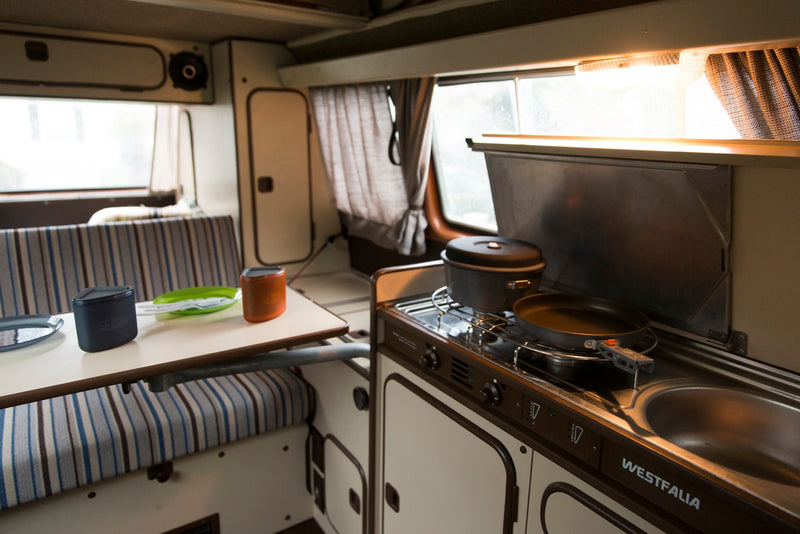 Cozy Westfalia RV rental interior: compact kitchen with stove, sink, and dining area. Perfect for camping trips! — photo 5