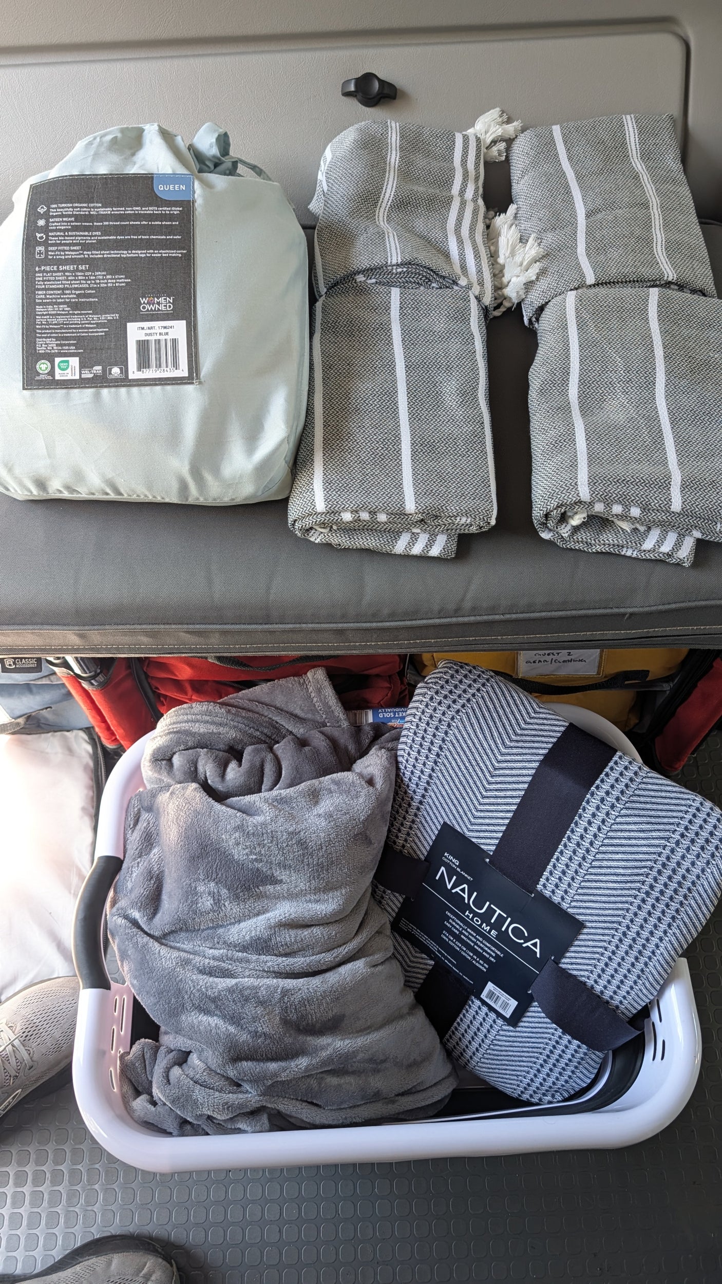 Preparing an RV rental with cozy bedding: a queen sheet set, striped blankets, and a plush blanket for travel comfort.