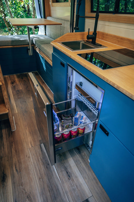 RV rental: functional kitchen with blue cabinets, bamboo counters, sink, cooktop, and a stocked fridge drawer. Dining area too.