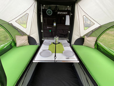 Explore this cozy RV rental interior. It features a dining table, comfortable green beds, and organized storage for your next camping trip.
