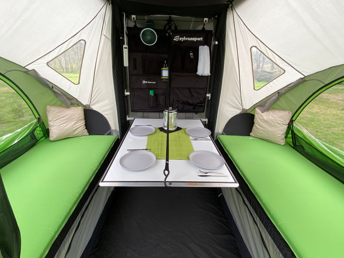 Explore this cozy RV rental interior. It features a dining table, comfortable green beds, and organized storage for your next camping trip.