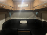 Cozy RV rental interior: black convertible seating/bed, overhead wood cabinets, and 'happily ever after' sign.