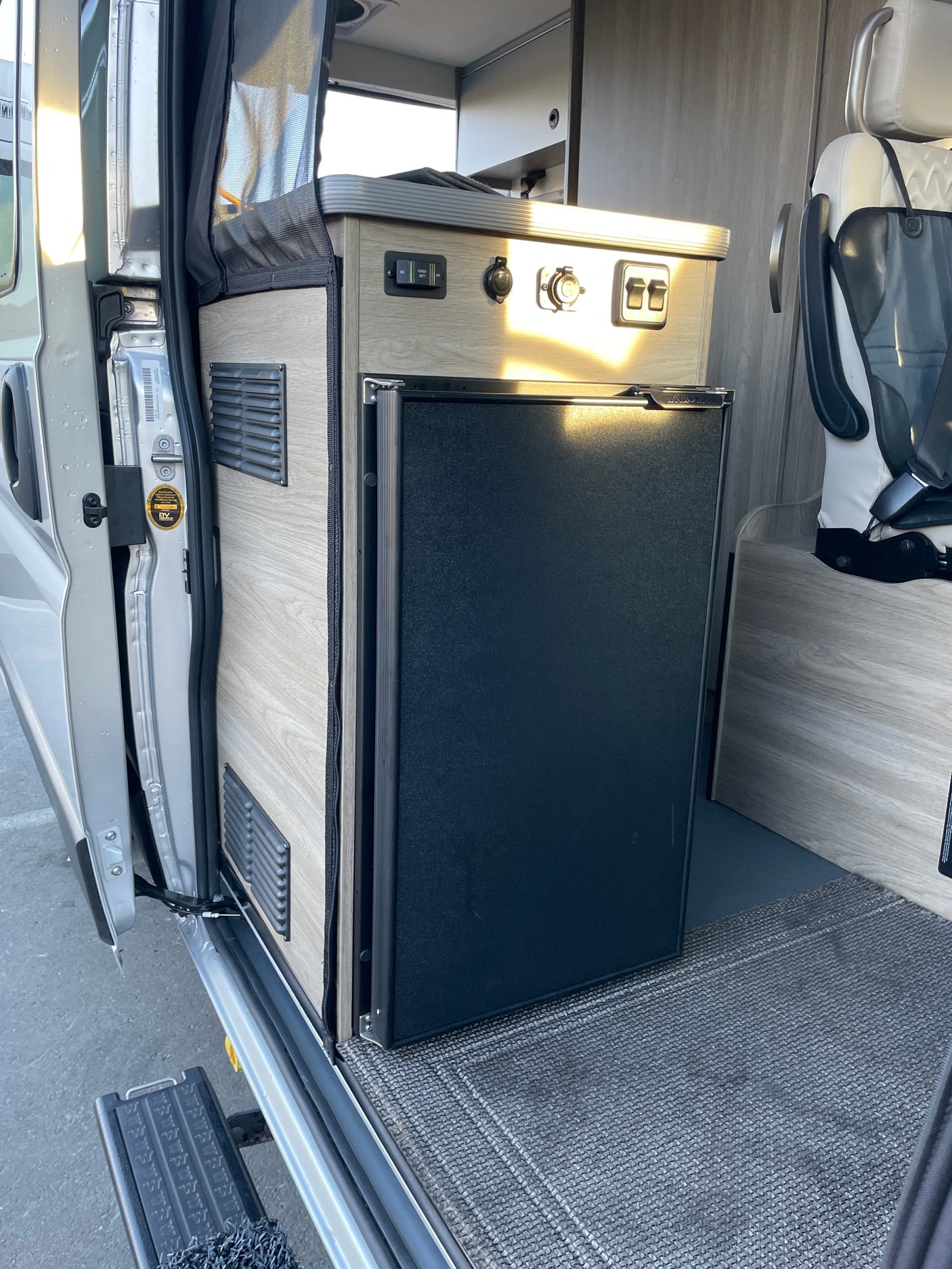 RV rental: Camper van interior featuring a built-in refrigerator, control panel, and screen near the side door.
