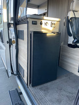 RV rental: Camper van interior featuring a built-in refrigerator, control panel, and screen near the side door.
