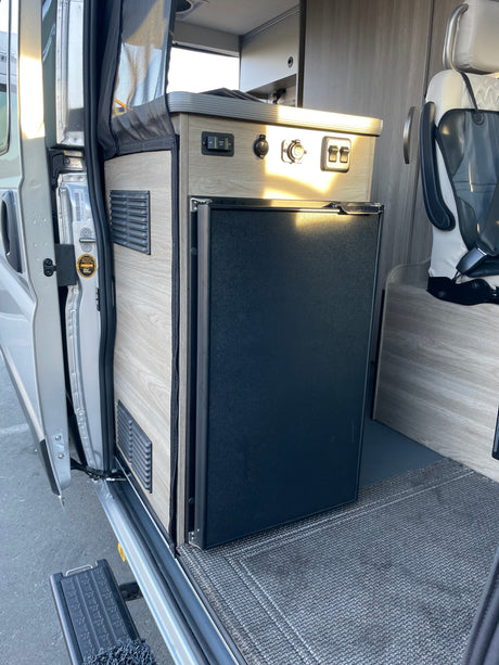 RV rental: Camper van interior featuring a built-in refrigerator, control panel, and screen near the side door.