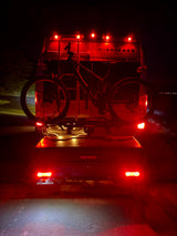 An RV rental at night, with a mountain bike on a Yakima rack and cargo box attached, illuminated by bright red taillights.
