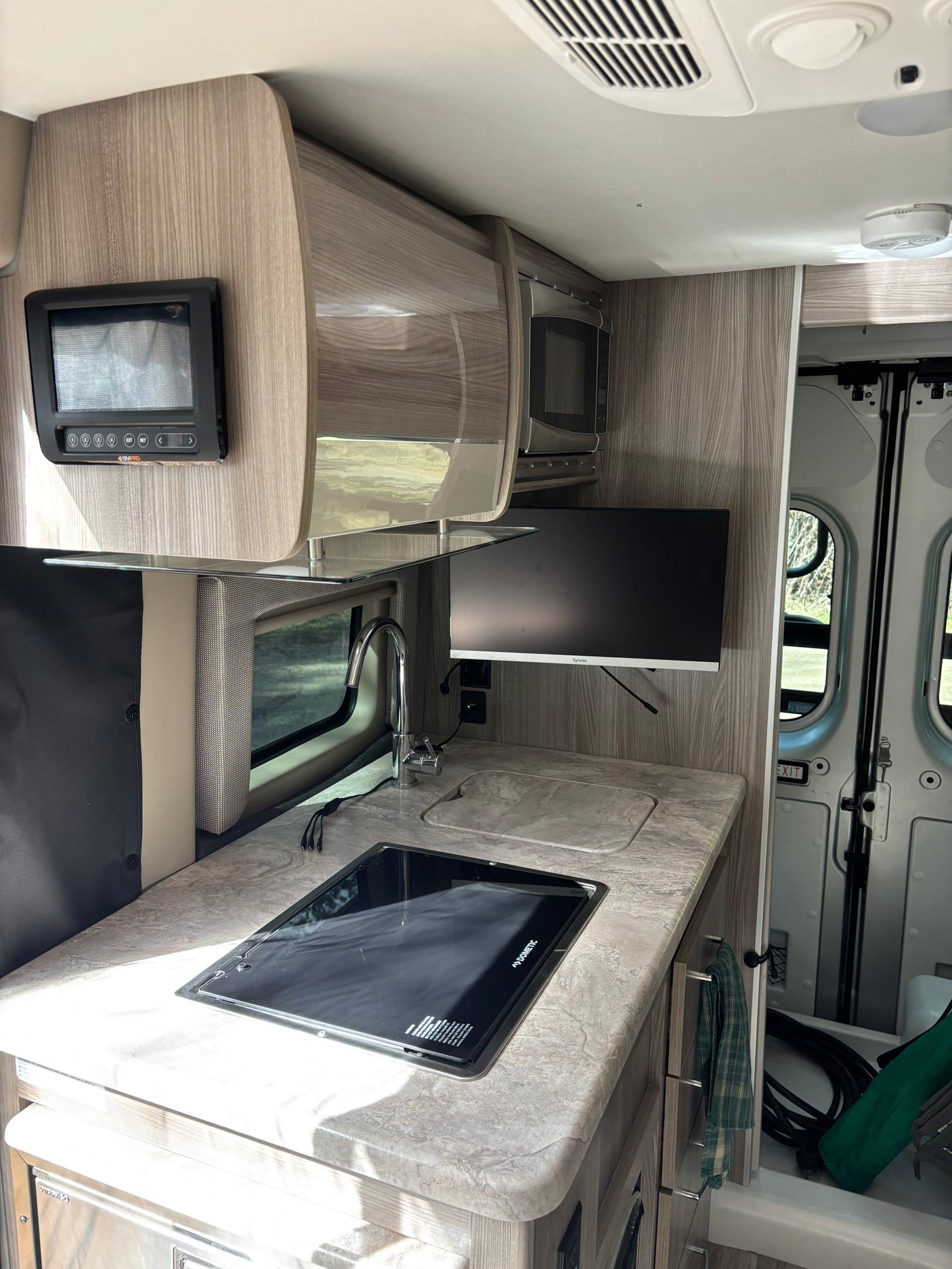 RV rental interior: a compact kitchen with Dometic stovetop, sink, microwave, and control panel, ideal for road trips.