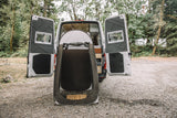 An RV rental's rear opens to a grey portable shower tent on gravel. Perfect for outdoor camping and privacy.