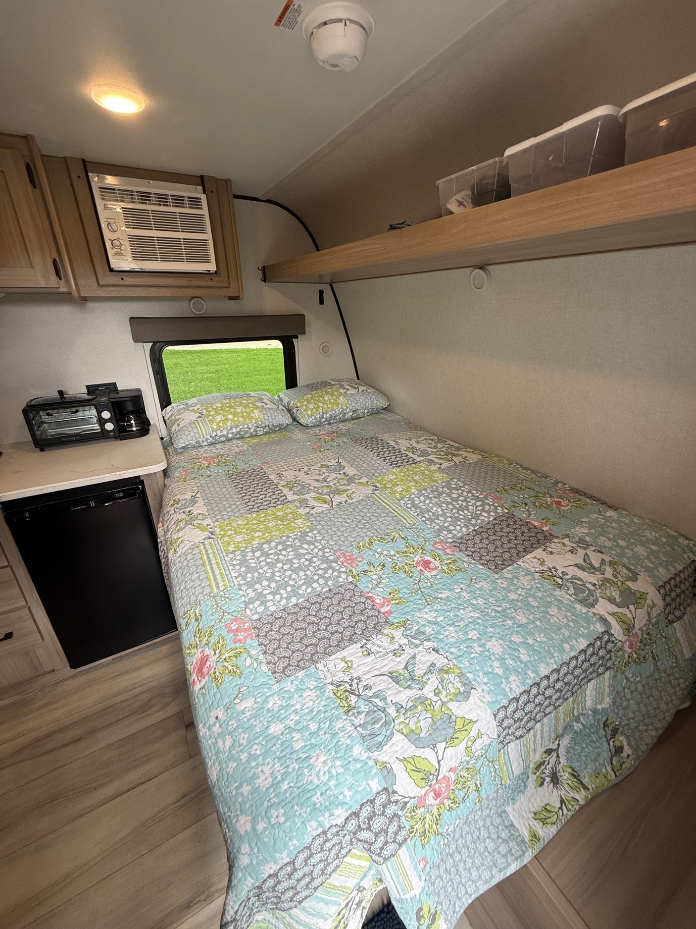 Cozy rv rental: a bedroom and kitchenette area with a colorful quilt, compact AC, mini-fridge, and toaster oven combo.