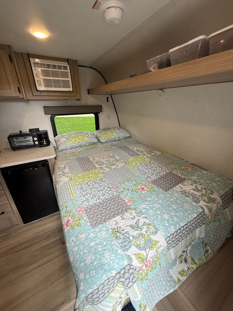 Cozy rv rental: a bedroom and kitchenette area with a colorful quilt, compact AC, mini-fridge, and toaster oven combo.