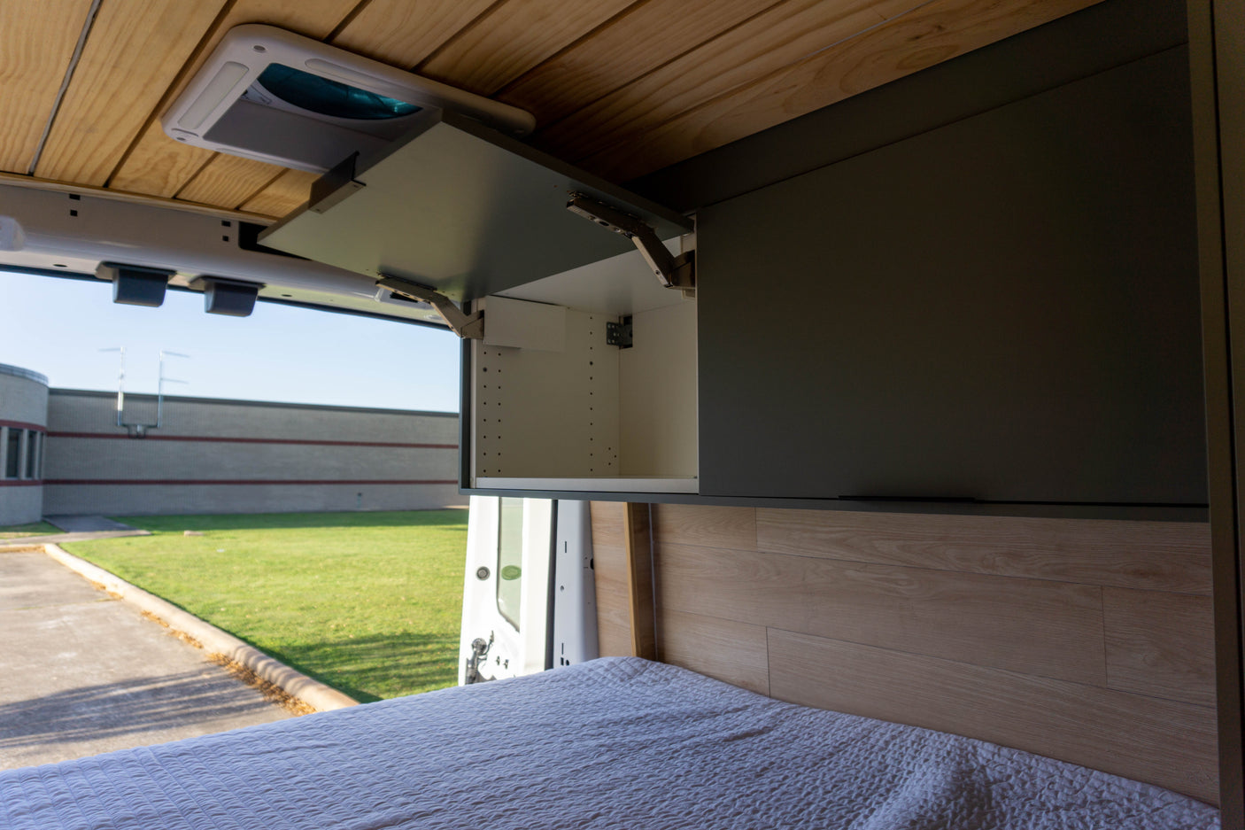 Spacious camper van rv rental interior with wooden ceiling, open overhead cabinet, and comfortable bed with outdoor view.