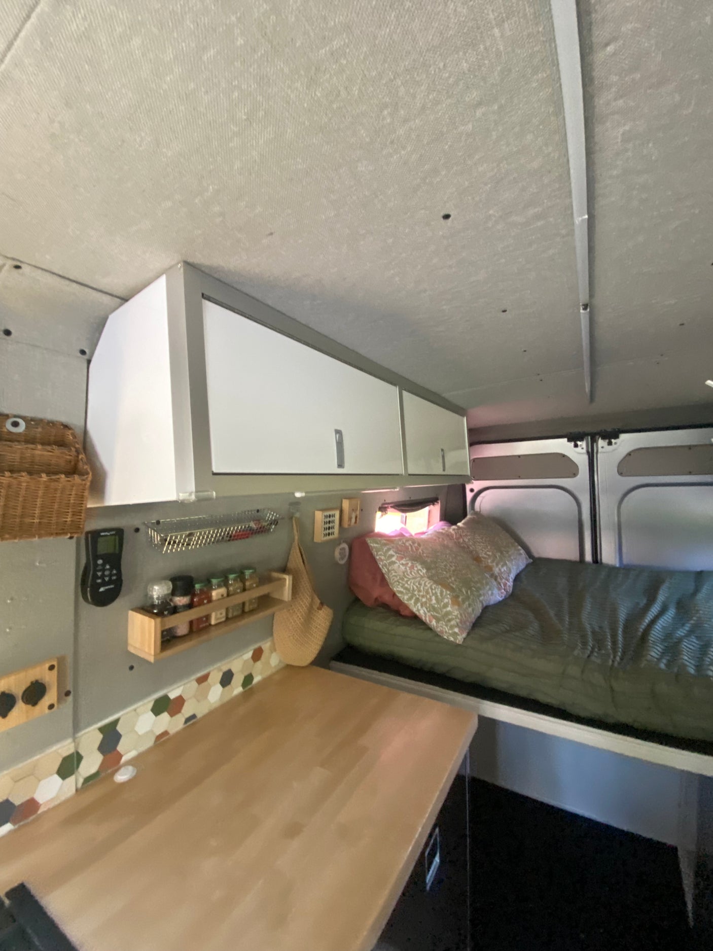 Cozy RV rental campervan interior: features overhead storage, a comfortable bed, and a functional kitchen counter.