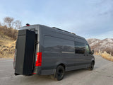 Dark gray adventure van, like an rv rental, with rear storage & roof rack. Parked by snowy mountains, ready for road trips.
