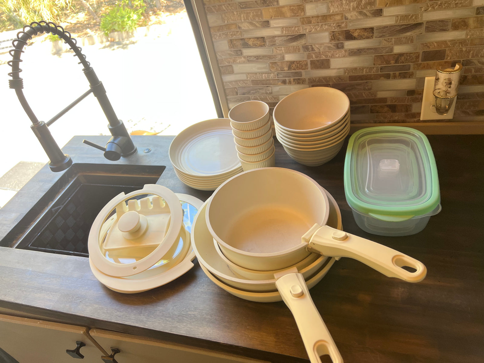 RV rental kitchen with stacked cream dishes, pots with detachable handles, and food storage, ready for cooking and meals.