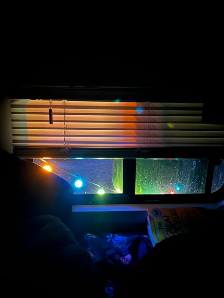 Cozy RV rental interior at night. Rain on the window, colorful string lights, and a book waiting to be read.